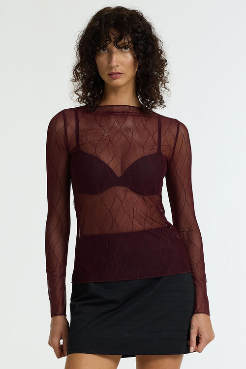 Woman wearing a sheer burgundy top and black skirt on a white background