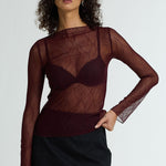 Woman wearing a sheer burgundy top with long sleeves and a black skirt on a white background