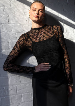 Person wearing a black lace top against a white brick wall