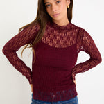 Woman wearing a burgundy lace top and blue jeans on a white background