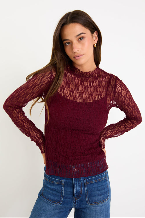 Woman wearing a burgundy lace top and blue jeans on a white background