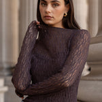 Woman wearing a dark brown sweater and blue jeans standing in front of classical architecture.