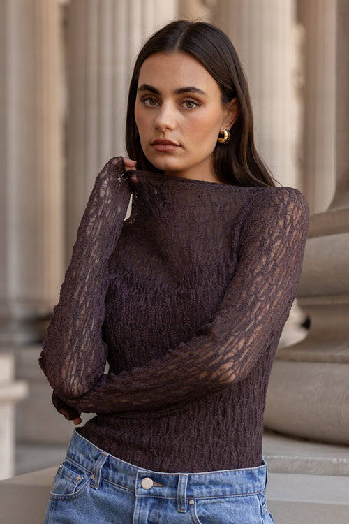 Woman wearing a dark brown sweater and blue jeans standing in front of classical architecture.