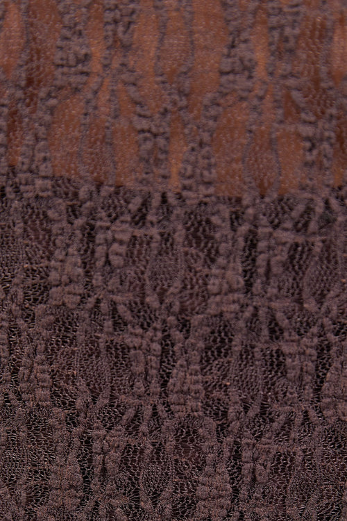 A woman wearing a fitted long-sleeve chocolate-brown lace top with a square neckline, paired with dark blue high-waisted jeans.