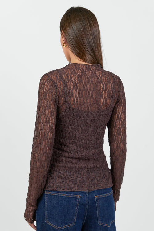 A woman wearing a fitted long-sleeve chocolate-brown lace top with a square neckline, paired with dark blue high-waisted jeans.
