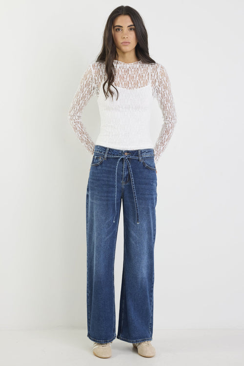 Woman wearing a white lace top and blue jeans on a white background