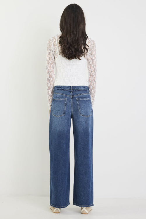 Person wearing blue jeans and a white top with lace sleeves on a white background