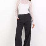 Woman wearing a white lace top and black pants on a white background