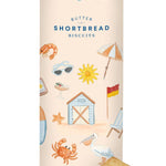 A cylindrical tin of Butter Shortbread Biscuits with a cream-colored label decorated with beach-themed illustrations, with two golden-brown biscuits placed in front on a white background.