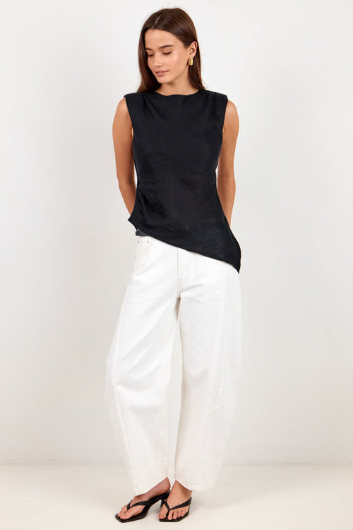 A woman modeling a sleeveless black top and white wide-leg pants with black sandals, standing against a plain light gray studio background.