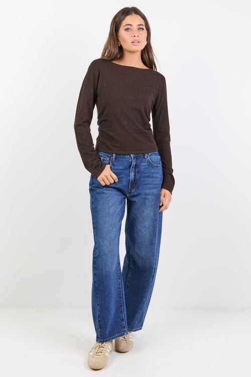 Woman wearing a brown long-sleeve top and blue jeans on a white background