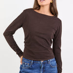 Woman wearing a brown long-sleeve top and blue jeans on a white background