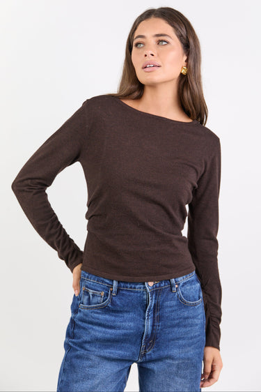Woman wearing a brown long-sleeve top and blue jeans on a white background