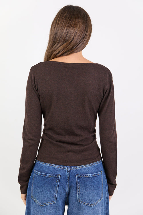 Person wearing a brown long-sleeve top and blue jeans on a white background