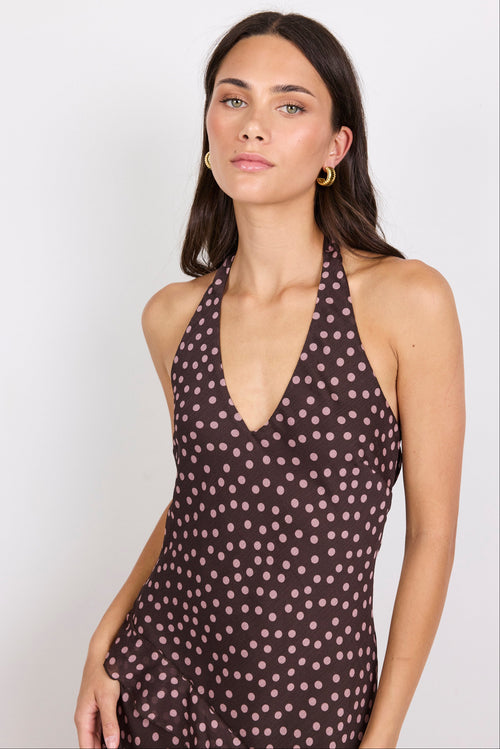 Woman wearing a brown halter maxi dress with pink polka dots on a white background.