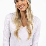 Woman wearing a gray knit beanie and white long-sleeve shirt on a white background