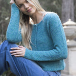 Woman wearing a teal sweater and blue jeans sitting outdoors.