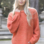 Woman wearing a coral sweater and blue jeans standing outdoors.