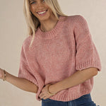 Woman wearing a pink knitted sweater and blue jeans against a beige background