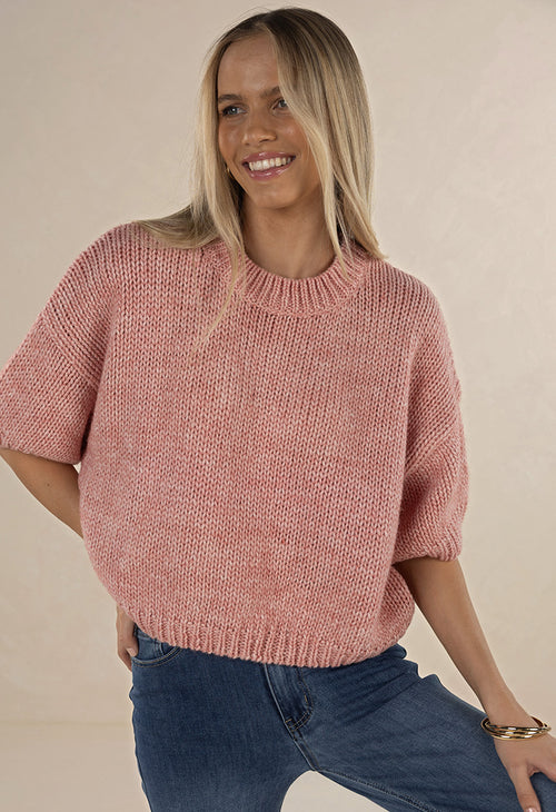 Woman wearing a pink knitted sweater and blue jeans against a beige background