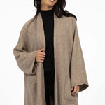 Woman wearing a beige coat over a black outfit on a white background