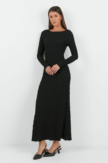 A woman wearing a long-sleeve black textured maxi dress with a fitted silhouette.