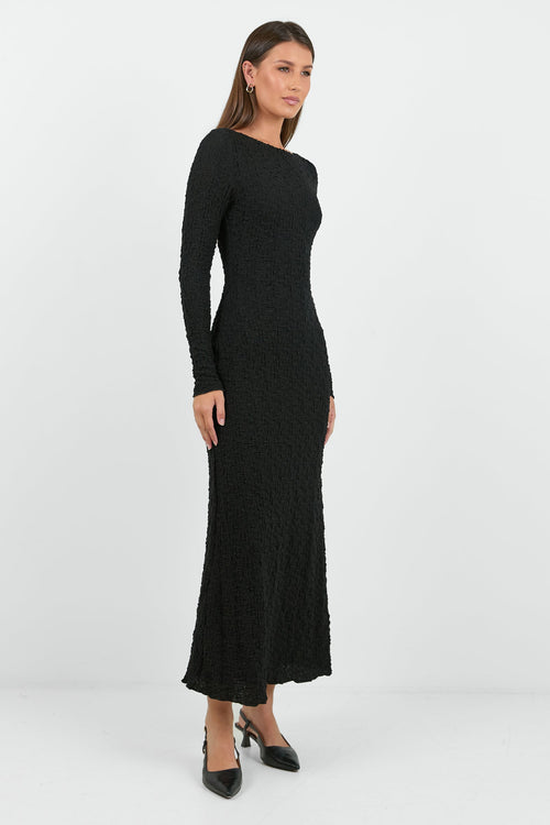 A woman wearing a long-sleeve black textured maxi dress with a fitted silhouette.