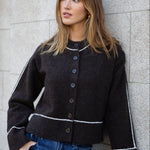 Woman wearing a black jacket with white trim against a gray wall.