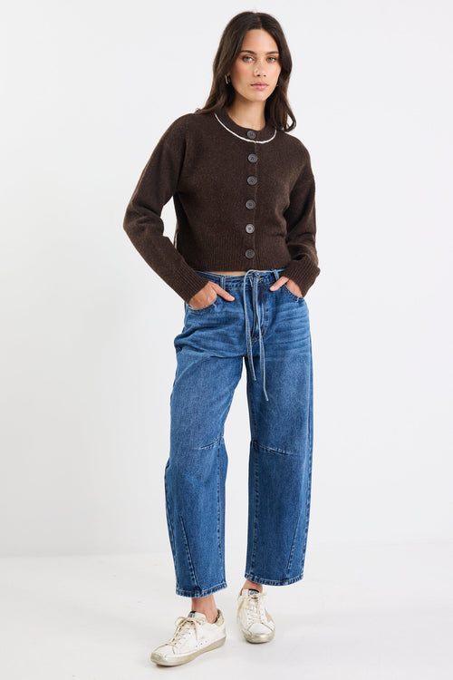 Woman wearing a brown cardigan, blue jeans, and white sneakers on a white background