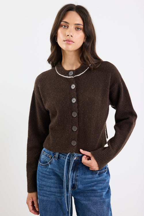 Woman wearing a brown cardigan and blue jeans on a white background