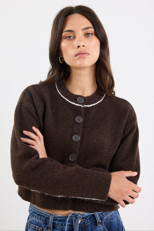 Woman wearing a brown cardigan with a white collar against a plain background