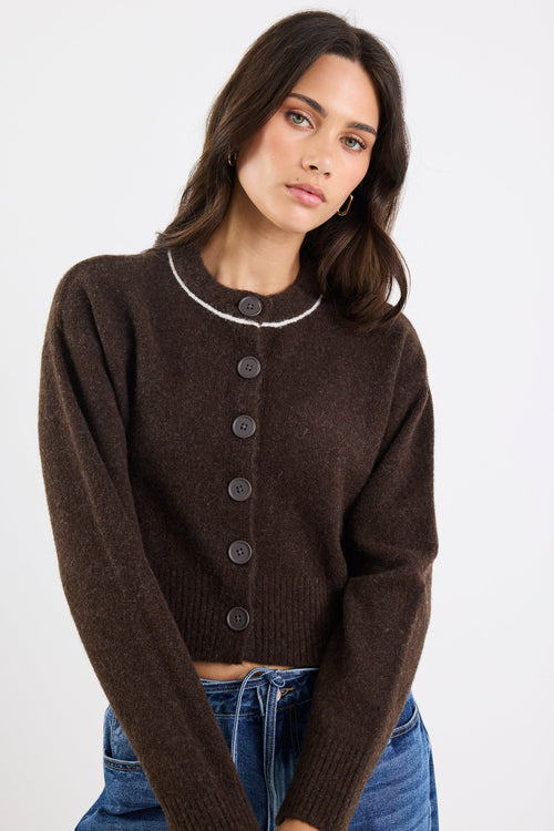 Woman wearing a brown cardigan with a white trim on a plain background
