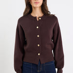 Woman wearing a brown cardigan with gold buttons on a white background