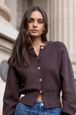 Woman wearing a brown cardigan and blue jeans standing in front of classical architecture.