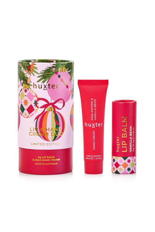 Huxter Lip & Hand Cream Duo Limited Edition set, featuring a cylindrical gift box with a pink and multicolor Christmas ornament design, a red lip balm tube, and a red lip balm tube with a matching patterned cap, on a white background.