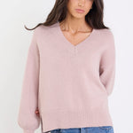 Woman wearing a pink sweater and blue jeans against a white background