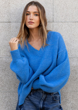 Woman wearing a blue sweater and jeans against a gray brick wall