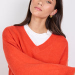 Woman wearing a orange sweater over a white shirt against a plain background
