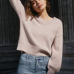 Woman in a light pink sweater and blue jeans standing in front of classical columns.