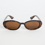 Slim oval tortoiseshell sunglasses with warm brown tinted lenses, photographed on a white background