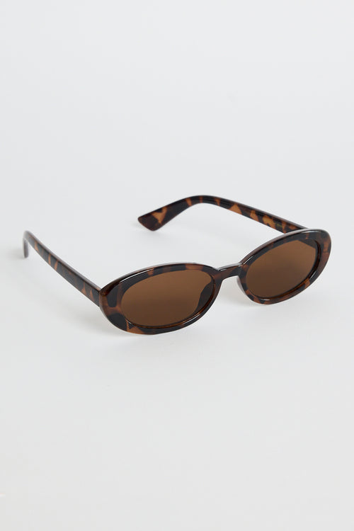 Slim oval tortoiseshell sunglasses with warm brown tinted lenses, photographed on a white background