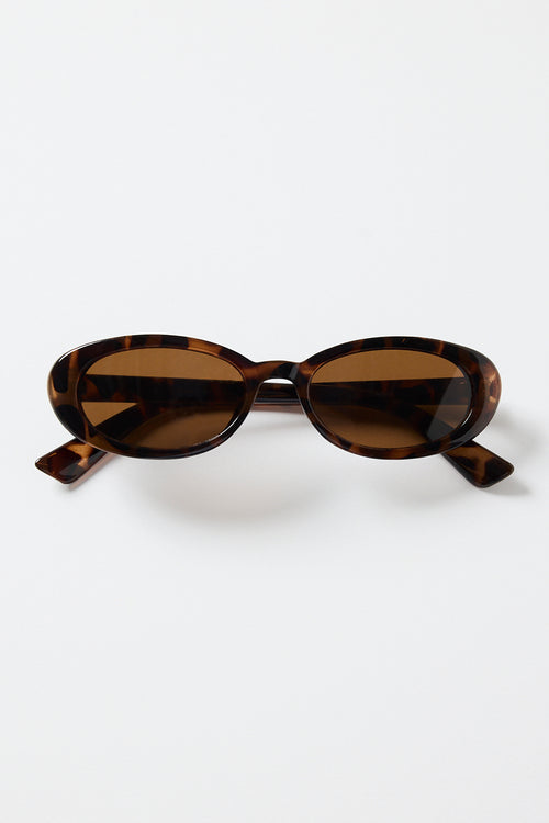Slim oval tortoiseshell sunglasses with warm brown tinted lenses, photographed on a white background