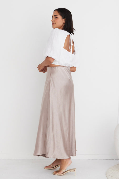model in white crop top and beige satin maxi skirt and heels