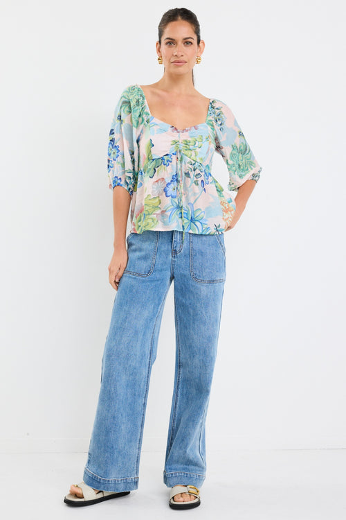 woman wearing a flowing floral puff sleeve dress with elastic waist and pastel blue and green print, styled with tan sandals.