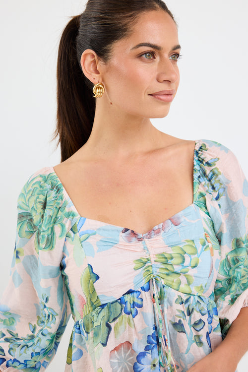 woman wearing a flowing floral puff sleeve dress with elastic waist and pastel blue and green print, styled with tan sandals.