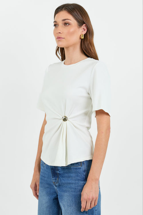 Woman wearing a white t-shirt with a twist and clasp detail and blue jeans on a white background