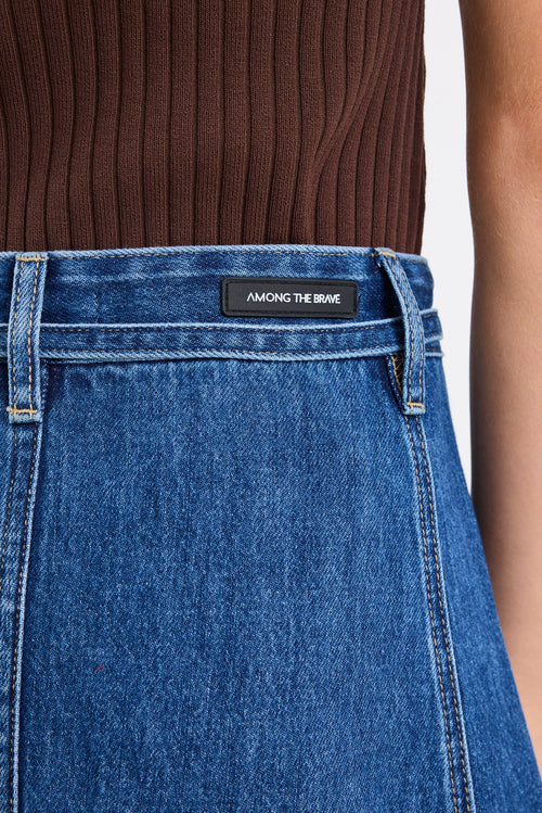 Close-up of blue jeans with a brand label on the waistband against a neutral background.