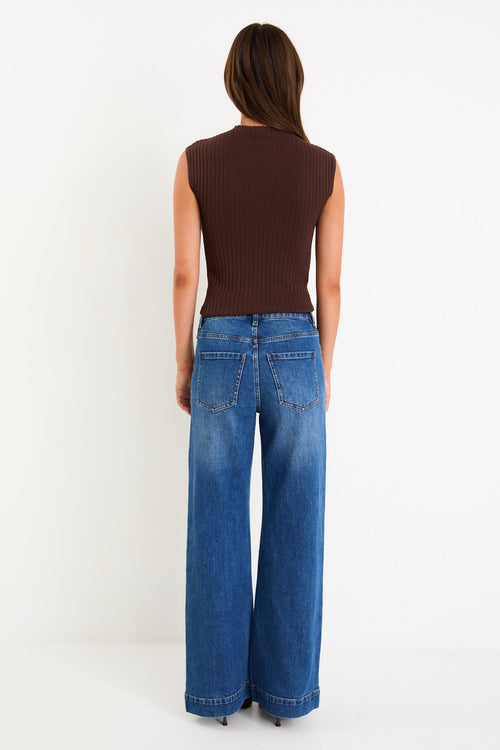 Person wearing a brown sleeveless top and blue jeans on a white background