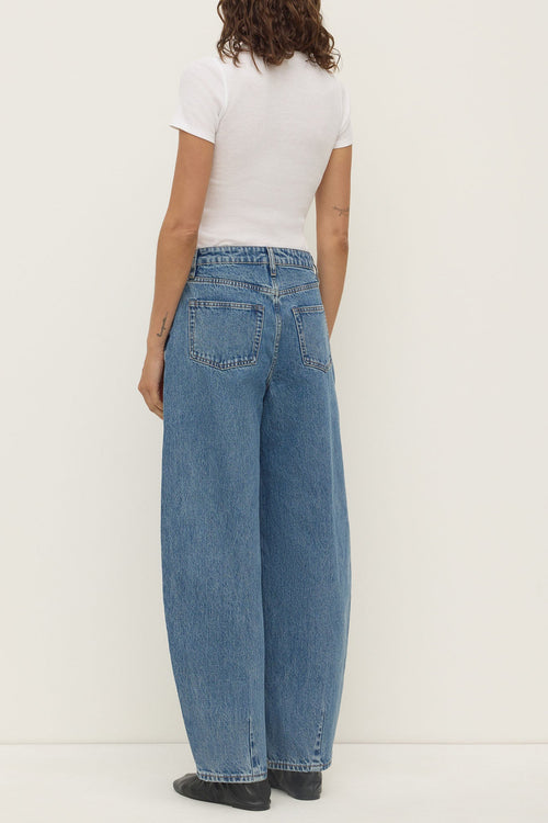 Person wearing blue jeans and a white top on a plain background