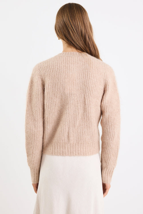 Woman wearing a beige sweater and white pants on a white background